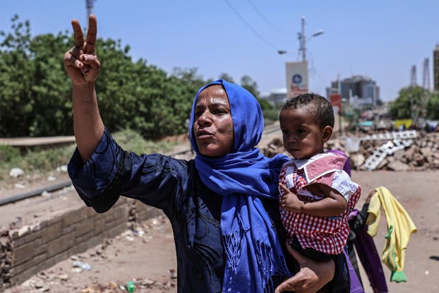 A protester flashes the victory sign while holding her child in a street leading to the sit-in outside the Sudanese military headquarters, in Khartoum, Sudan, Tuesday 14 May 2019.