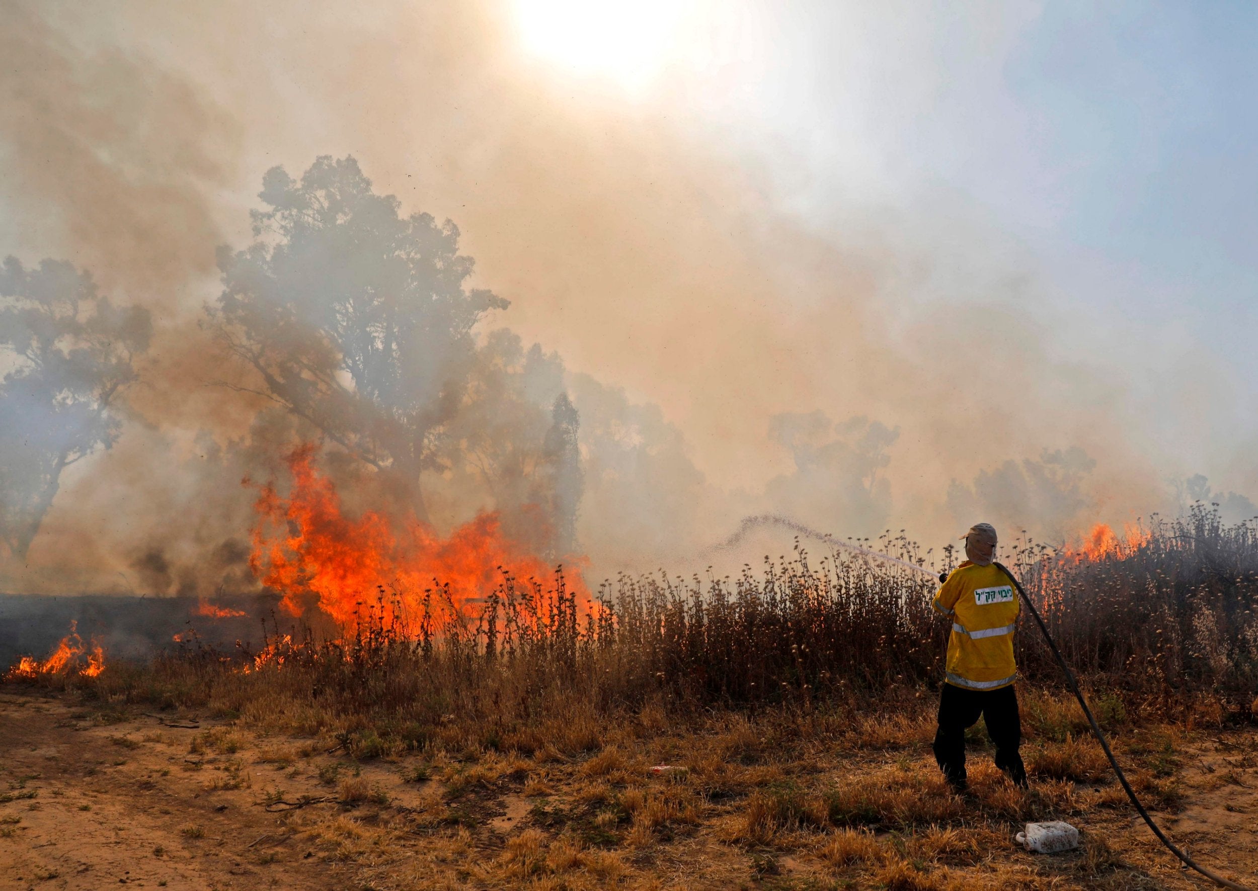 An Israeli fireman extinguishes a fire in a burning field next to Kibbutz Beeri, reportedly caused by inflammable material attached to kites and flown across the border to Israel from the Gaza Strip on 15 May 2019 (AFP/Getty)