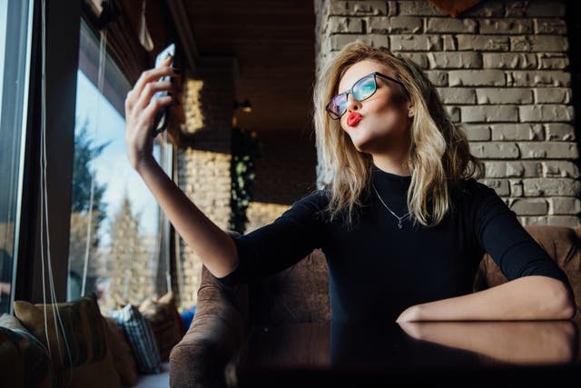 Woman taking a selfie in coffee shop. Hipster, red lips, glasses