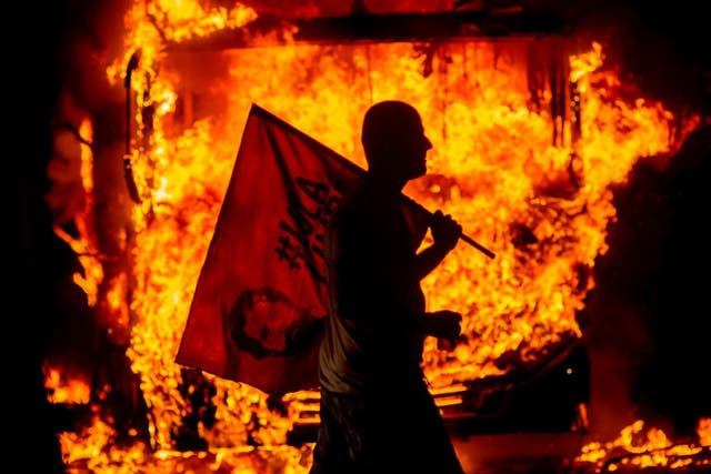 A man holds a flag and walks past a bus in flames during a protest