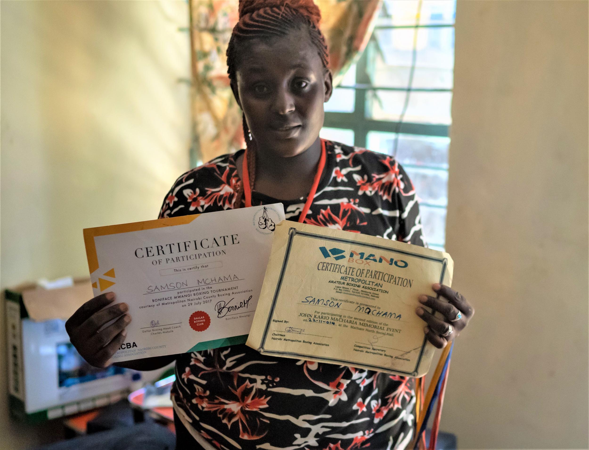 Purity Muchama holds up certificates awarded to her brother Samson, who was beaten to death