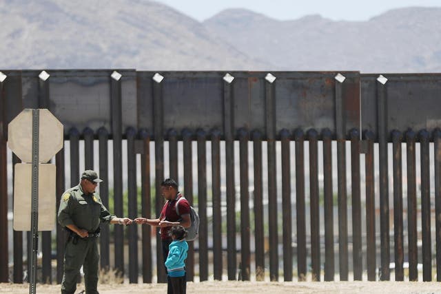 A US Border Patrol agent (L) checks the identification of a migrant with a child as they are detained after crossing to the US side