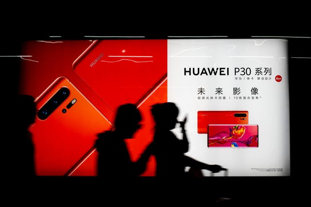 Commuters walk by the new Huawei P30 smartphone advertisement on display inside a subway station in Beijing Monday