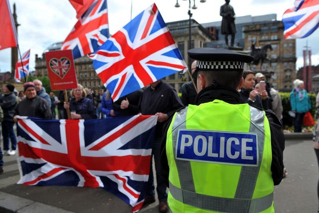 A police officer stands on duty near pro-Union demonstrators flying Union flags as they demonstrate against Pro-Scottish Independence activists marching through the streets of Glasgow during the All Under One Banner March for Independence on May 4, 2019