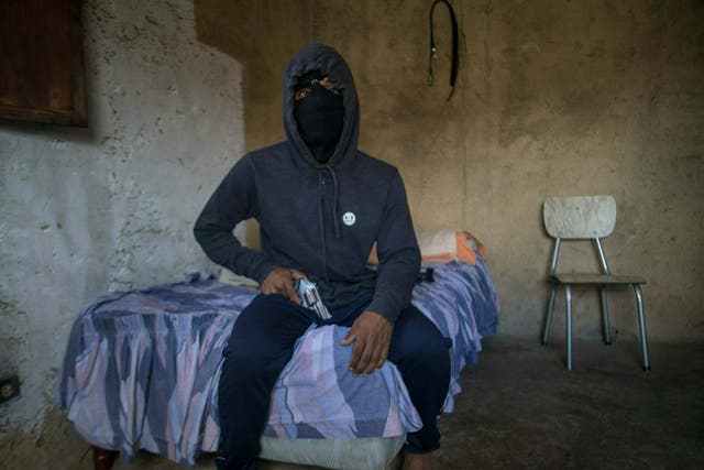 A masked gangster who goes by the nickname "El Negrito" poses for a portrait with his gun inside his gang's safe-house