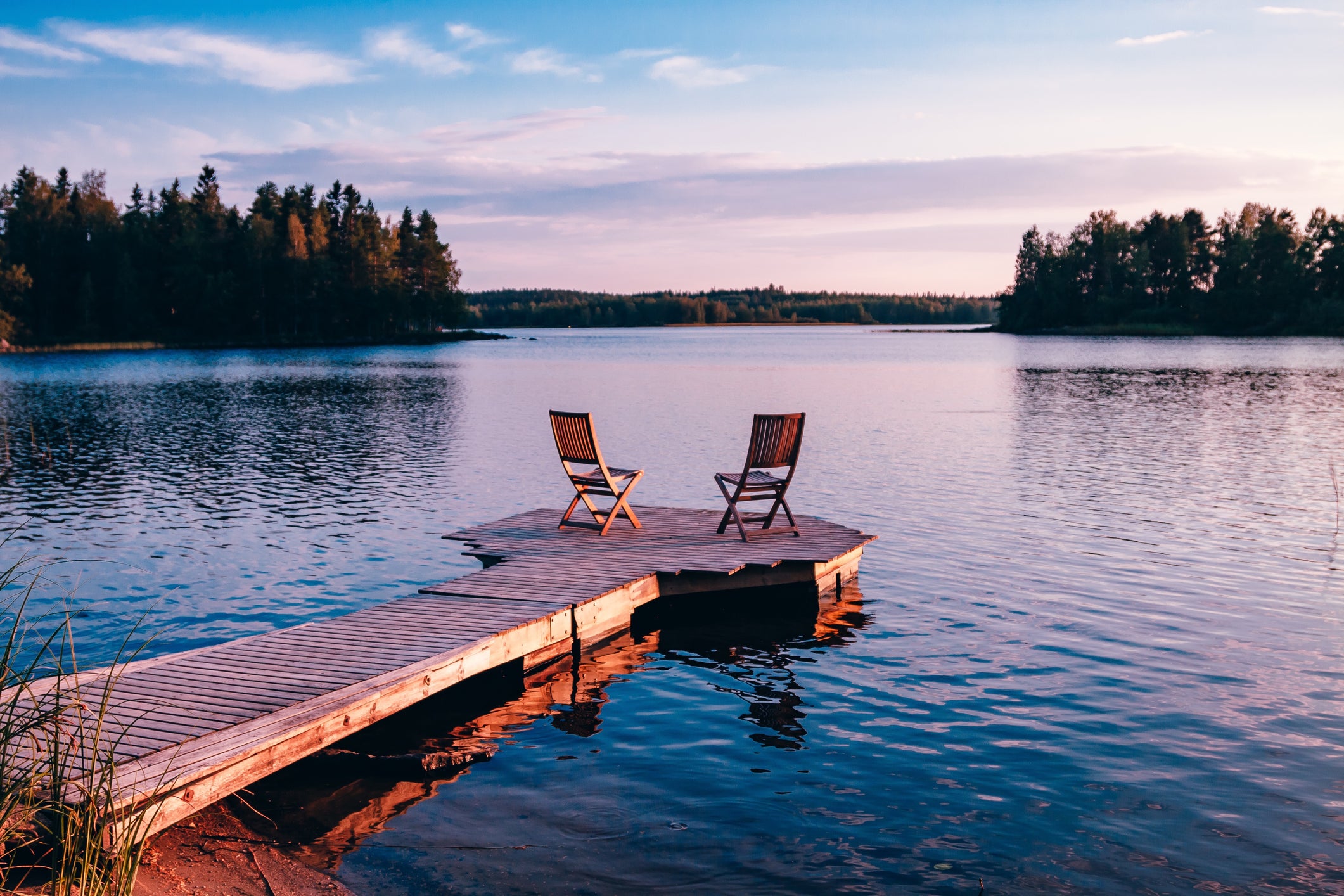 Two wooden chairs on a wood pier overlooking a lake at sunset in Finland