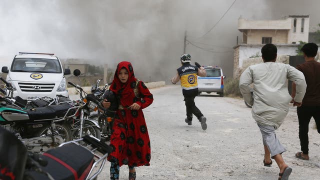 Syrians, including a member of the White Helmets civil defence rescue teams, run for cover during an air strike by pro-regime forces on the market town of Kfar Ruma in Syria's southwestern Idlib province, on May 30, 2019. - Regime forces and their Russian allies have over the past three months escalated bombardment of Syria's last major jihadist bastion in the province of Idlib and adjacent areas