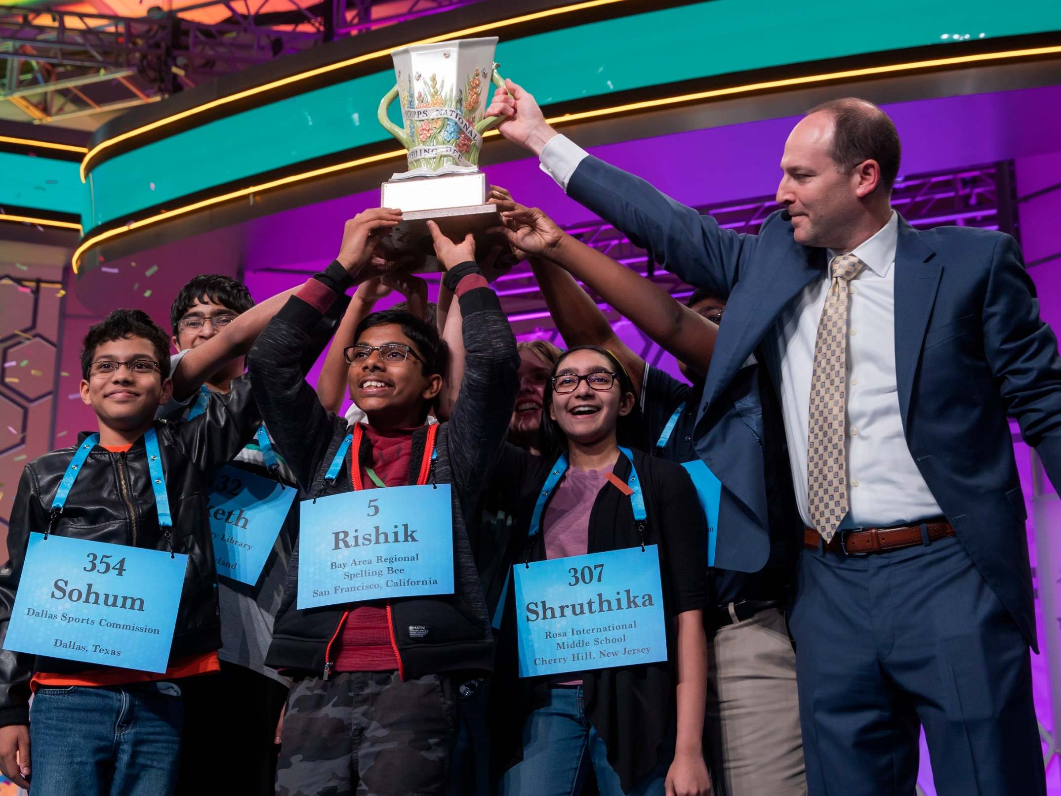 Scripps president and Chief Executive Officer Adam Symson (R) gives the trophy to the eight co-champions on the final day of the 2019 Scripps National Spelling Bee