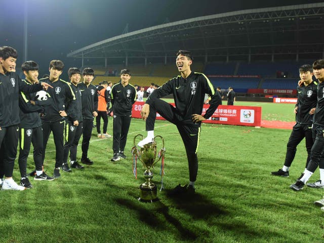 A member of South Korea Under-18s poses with his foot on the Panda Cup after their victory