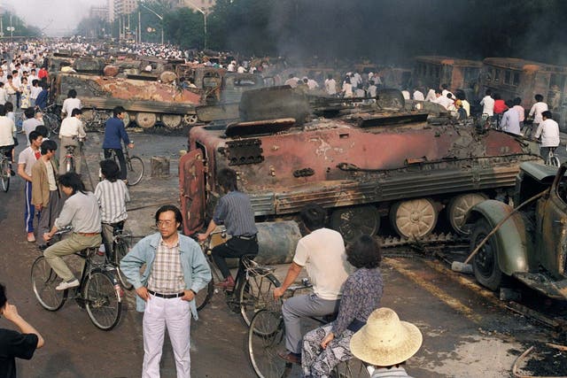 In this file photo taken on 4 June 1989, residents gather near the smoking remains of over 20 armoured personnel carriers burnt by demonstrators during clashes with soldiers near Tiananmen Square