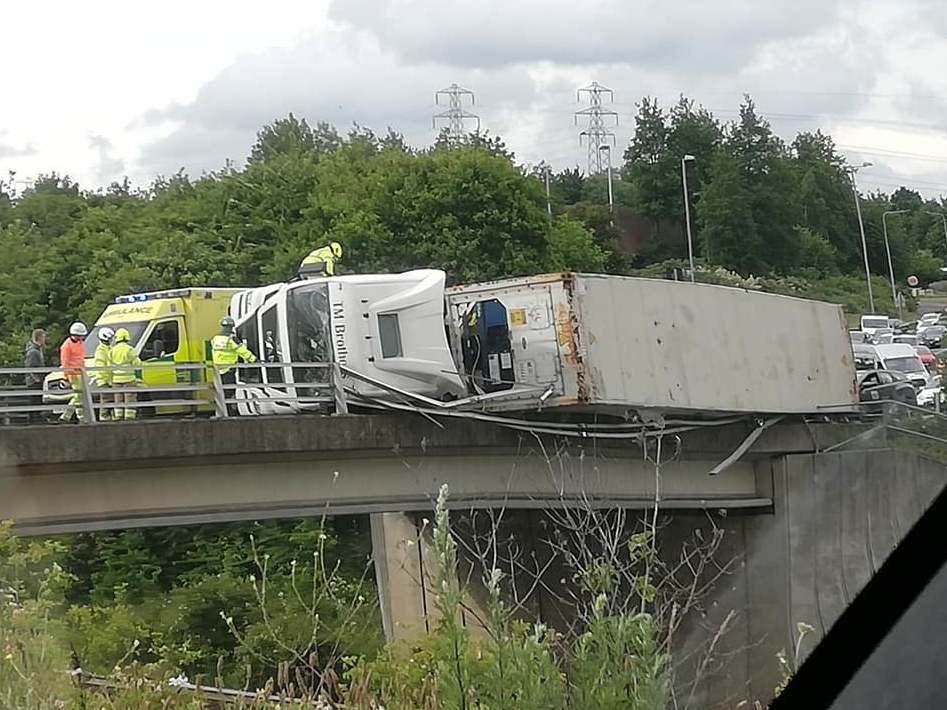 A lorry hangs over the edge of a bridge above a dual carriageway after overturning in Suffolk 7 June 2019.