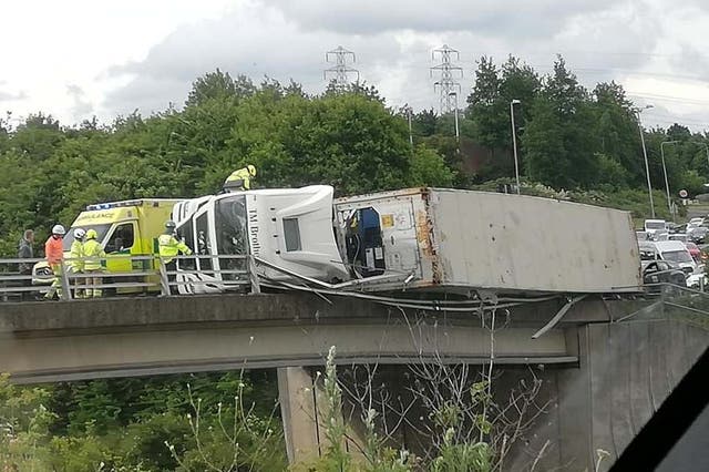 A lorry hangs over the edge of a bridge above a dual carriageway after overturning in Suffolk 7 June 2019.