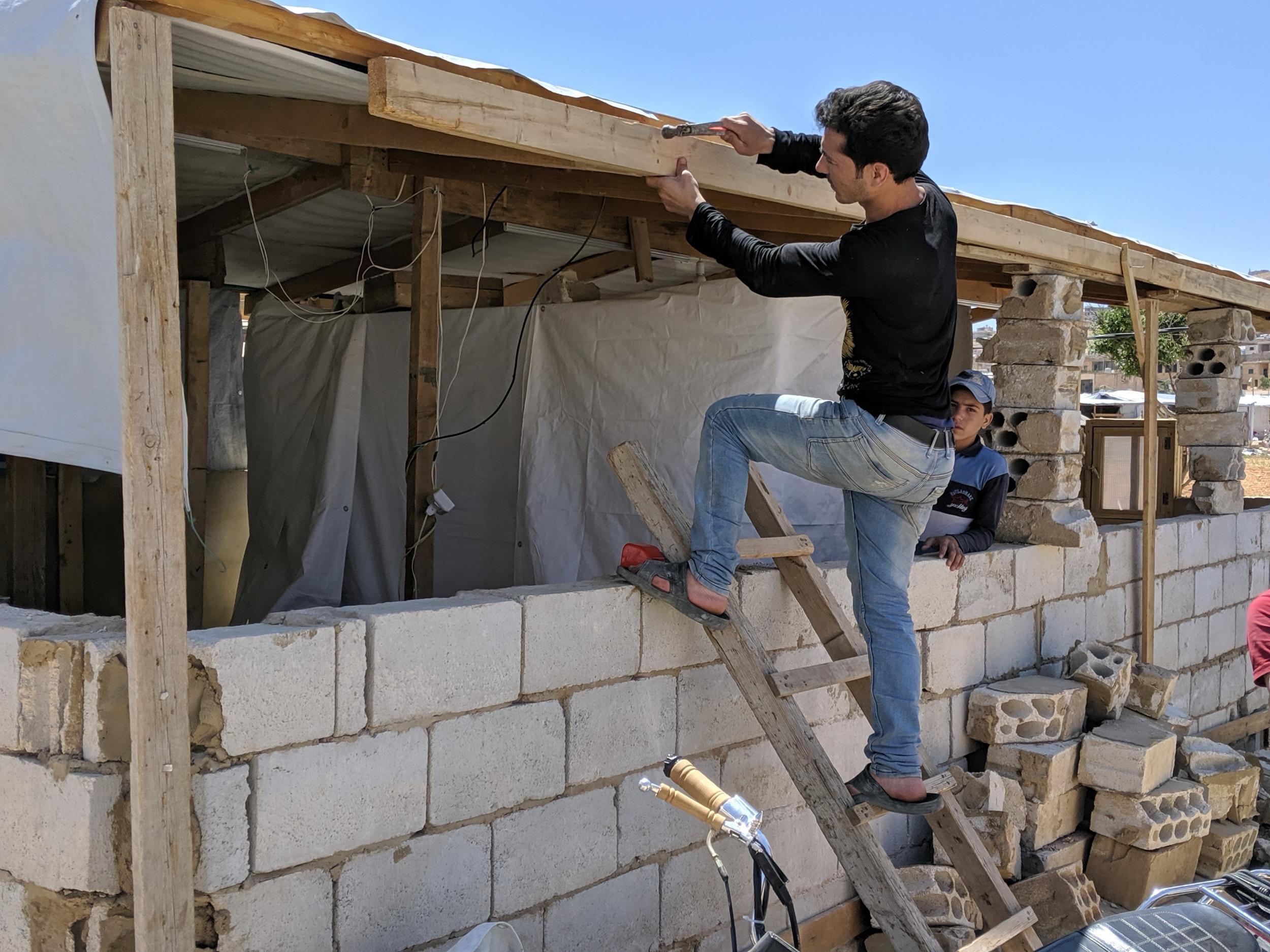 Syrian refugee Ali Shehadi, 28, fixes the roof of his shelter after removing half of the outer walls, at a camp in Arsal (Richard Hall/The Independent)