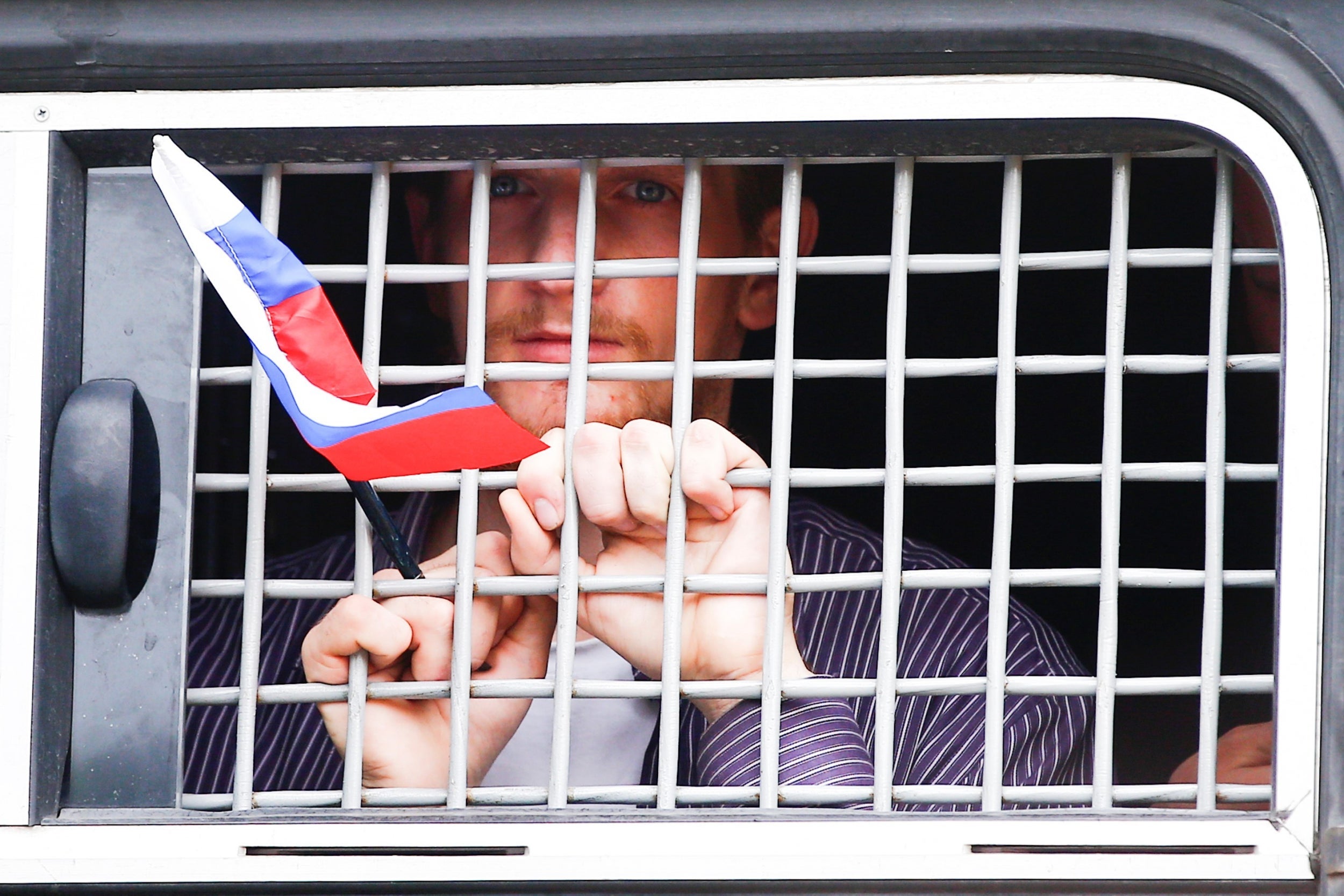 A detained protester holds a Russian flag while looking out of a police bus window during a march in Moscow