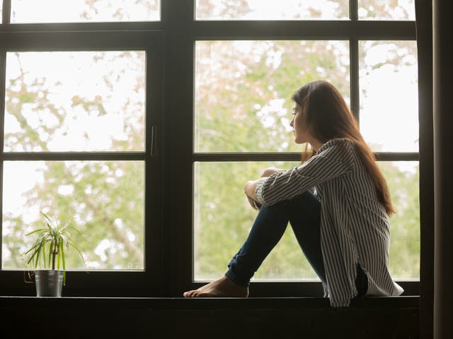 Girl sitting on sill embracing knees looking at window.