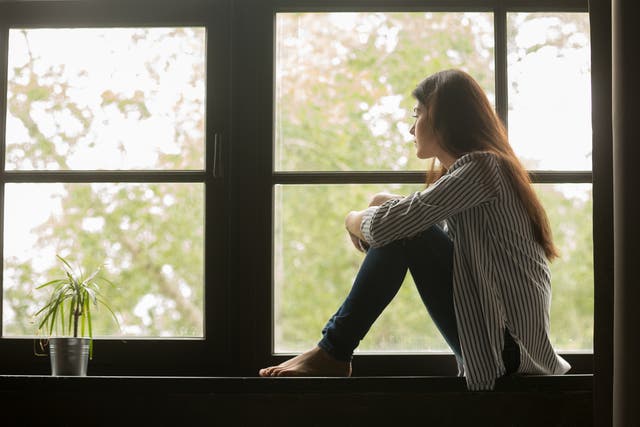 Girl sitting on sill embracing knees looking at window.