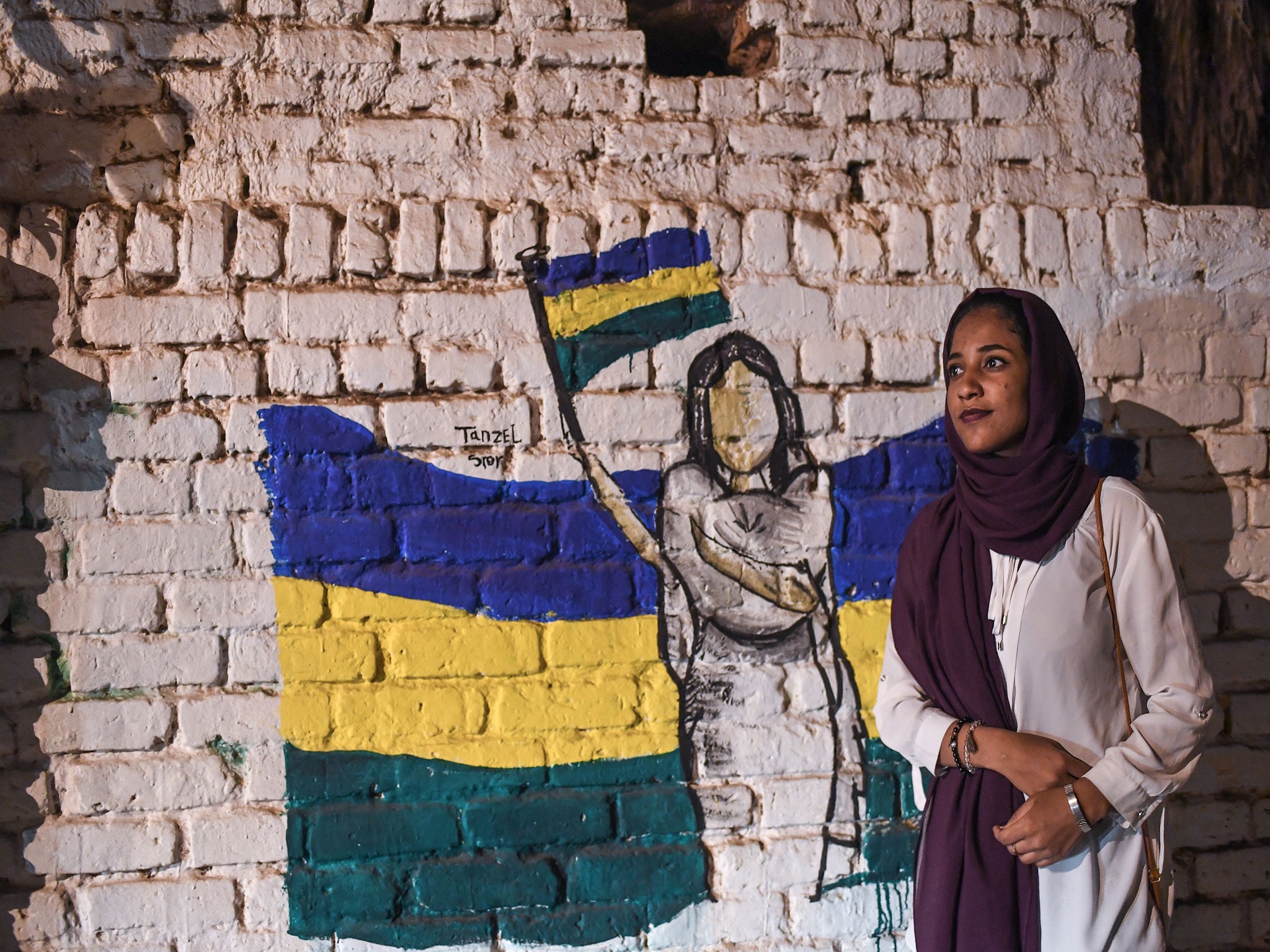 Sudanese protester, Alaa Salah, poses in front of a recently painted mural of a female protester