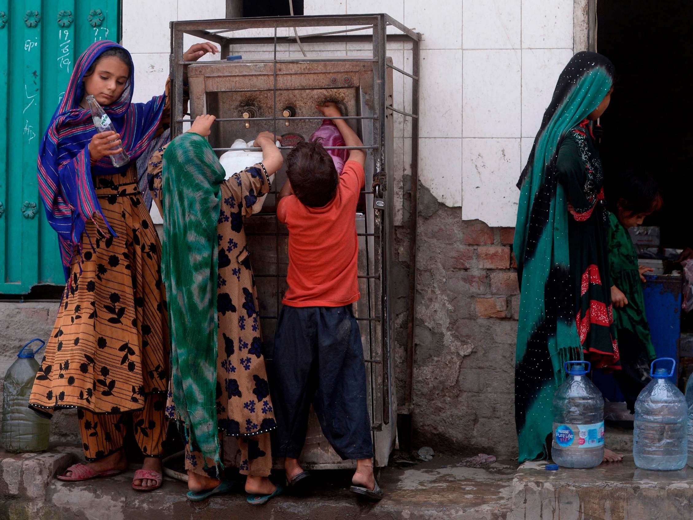 Afghan refugees fill water bottles near their makeshift houses in Lahore on 19 June 2019, ahead World Refugees Day on 20 June.