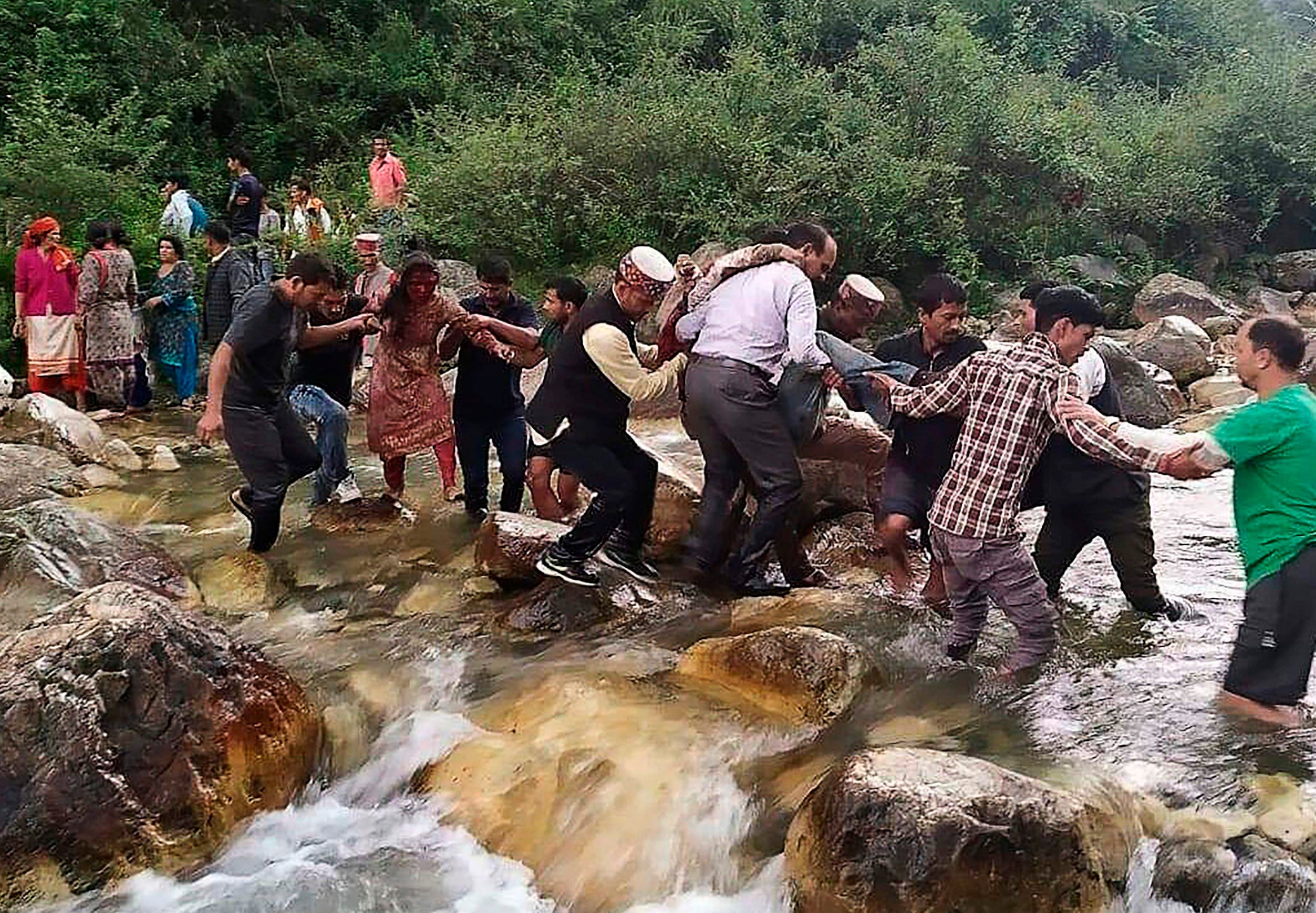 Local residents help accident survivors cross a river after a bus crash in the mountainous Kullu district of the Indian state of Himachal Pradesh