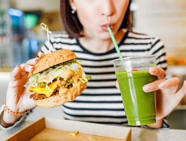 A woman in a vegan restaurant with a plant-based burger and smoothie.