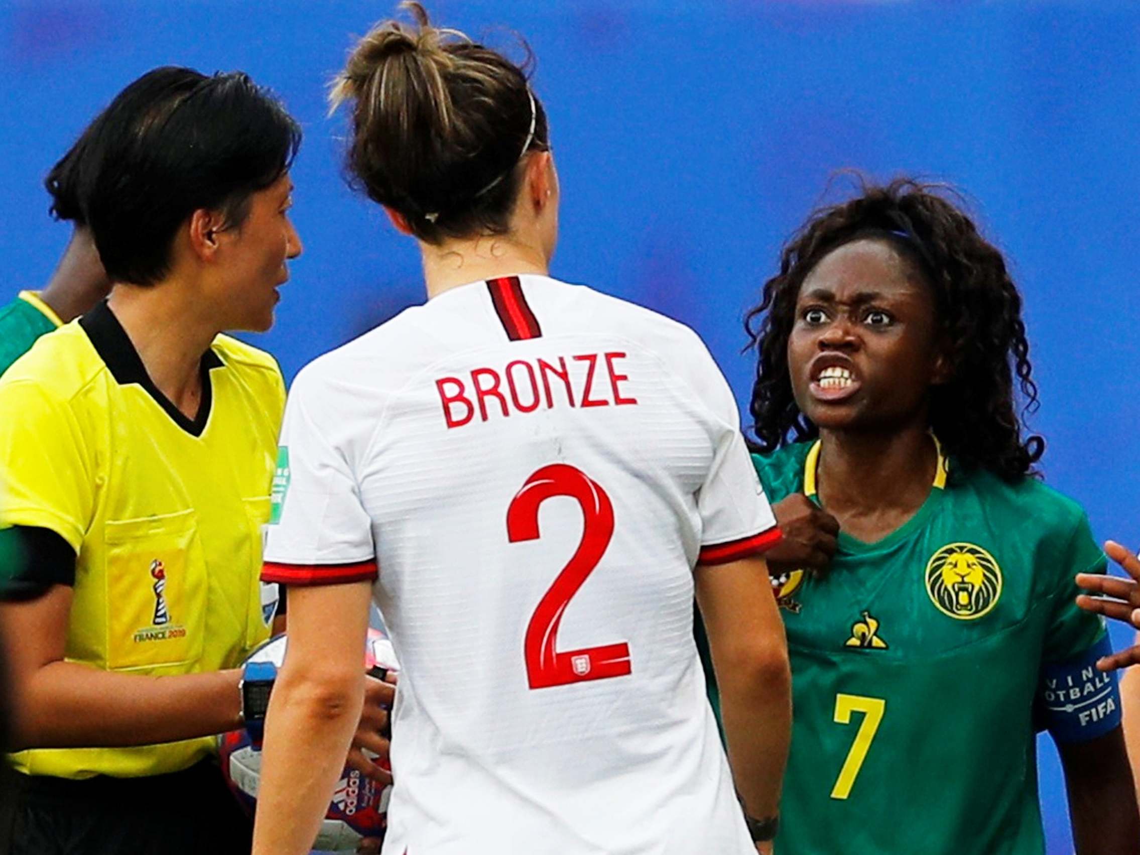 Cameroon's Gabrielle Onguene reacts at England's Lucy Bronze as referee Qin Liang looks on