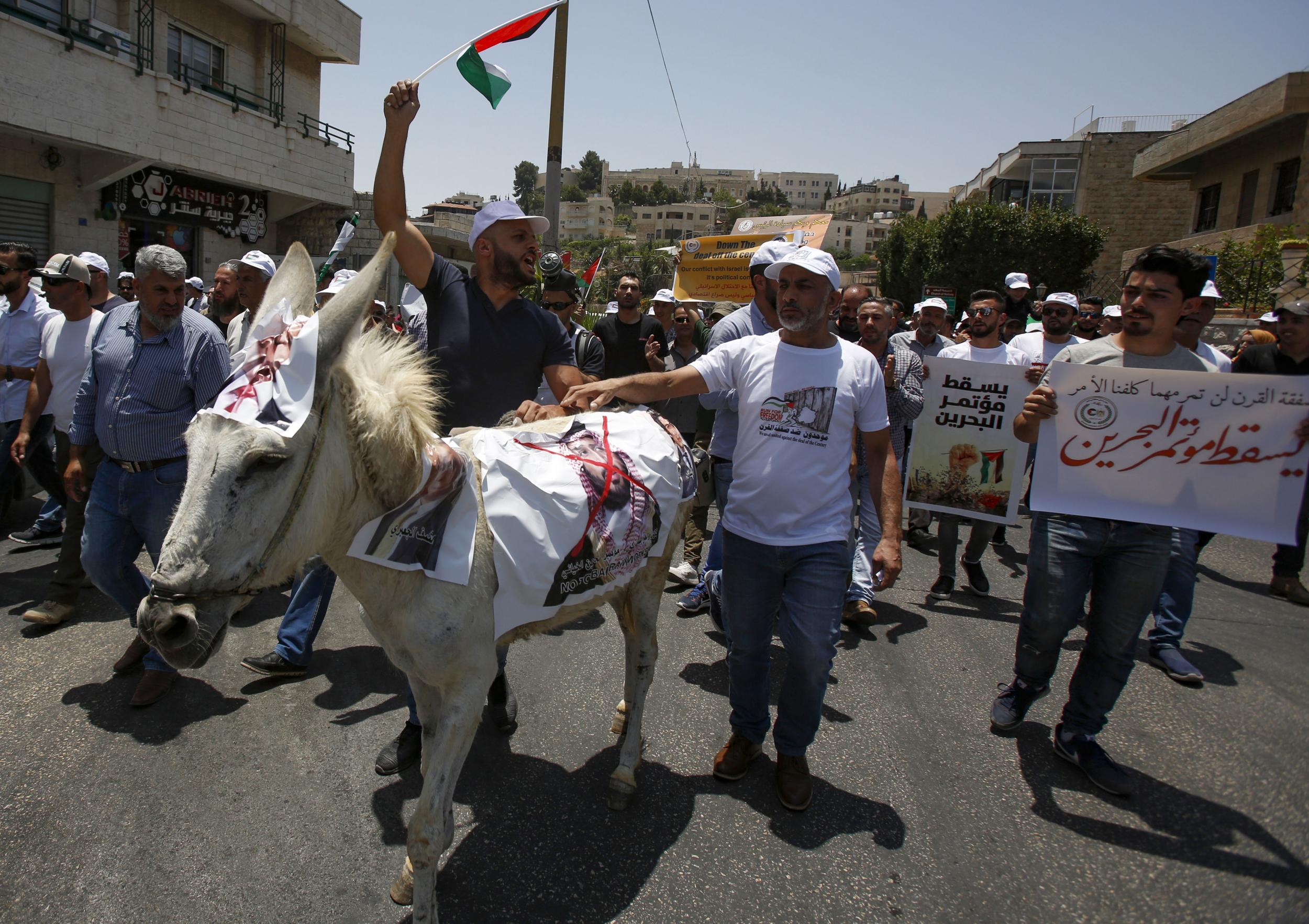 Palestinian demonstrators chant slogans as they walk along a donkey with a photograph of Crown Prince Mohammed bin Salman during protests against a US peace plan