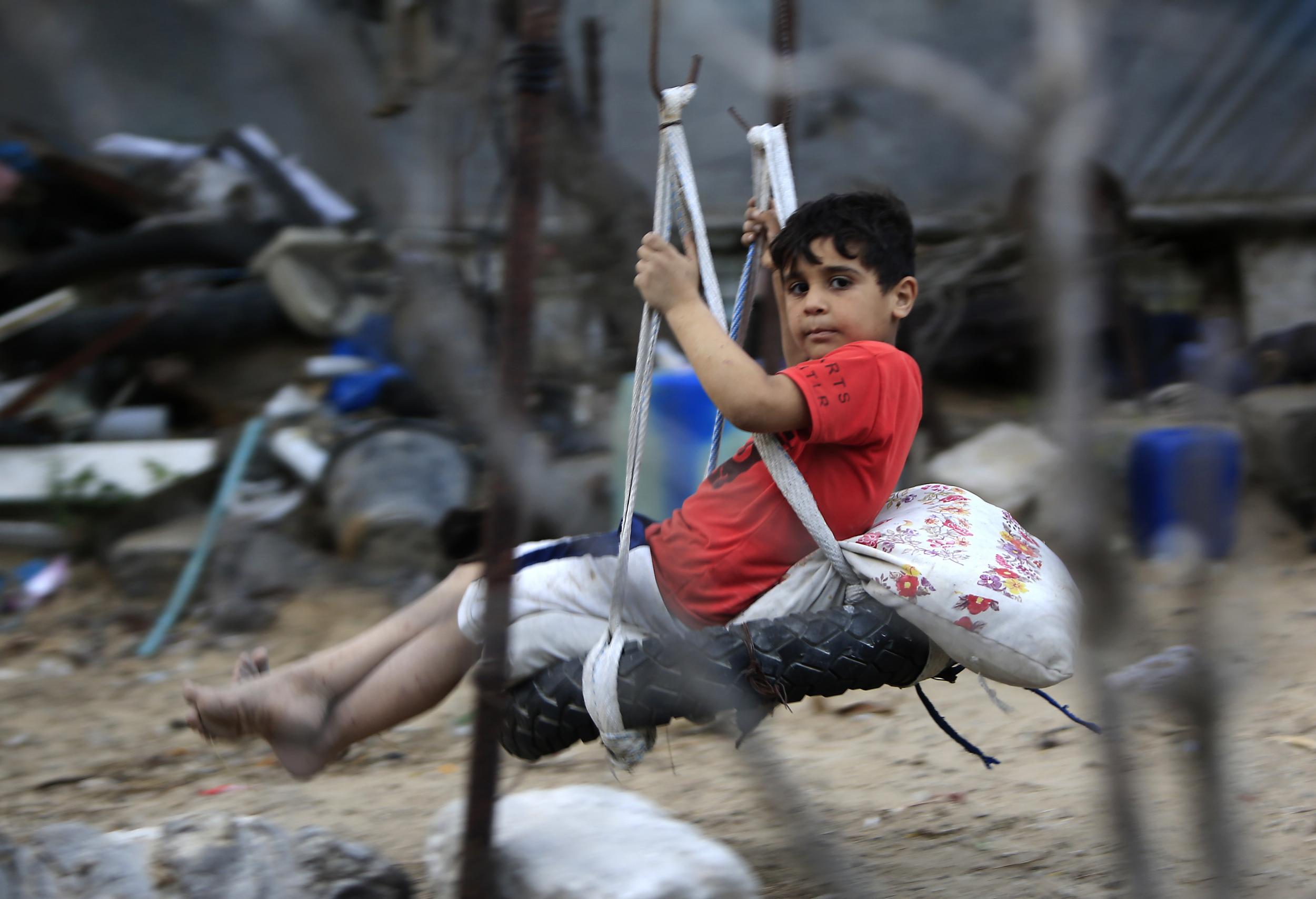 A Palestinian boy plays on a makeshift swing outside his house in a southern Gaza Strip refugee camp
