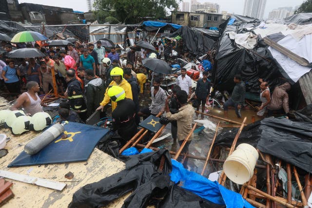 Rescue workers and locals stand near a damaged structure after a wall collapsed at the Pimpri Wada Malad East in Mumbai