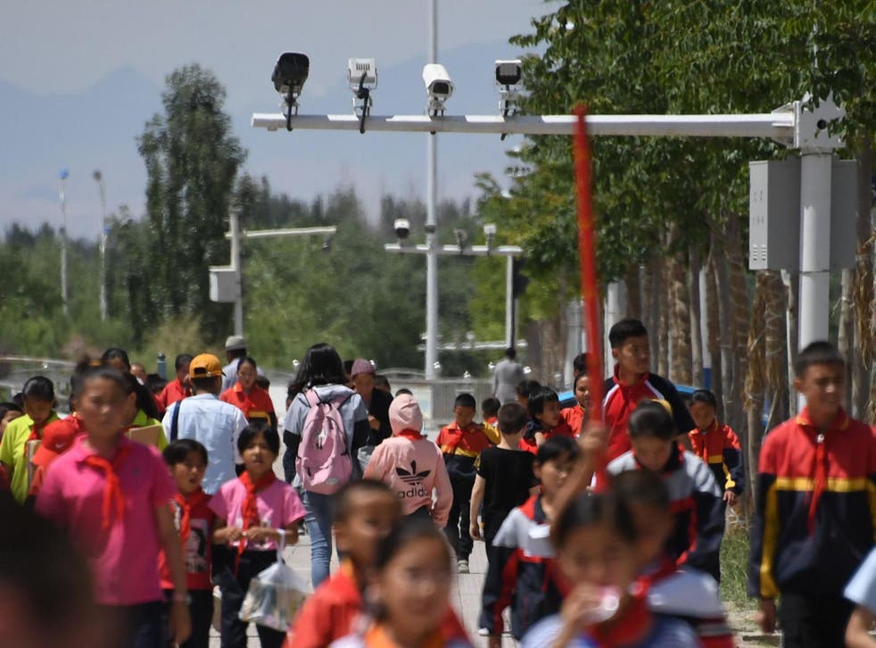 Children walk in shadow of surveillance cameras in heavily policed Xinjiang region, where Chinese officials are installing secret software into visitors' phones to gather data in crack down on Muslims' freedoms