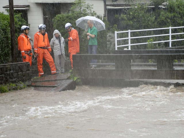 Rescue workers and local residents watch as the Wada River approaches its overflow level in Kagoshima