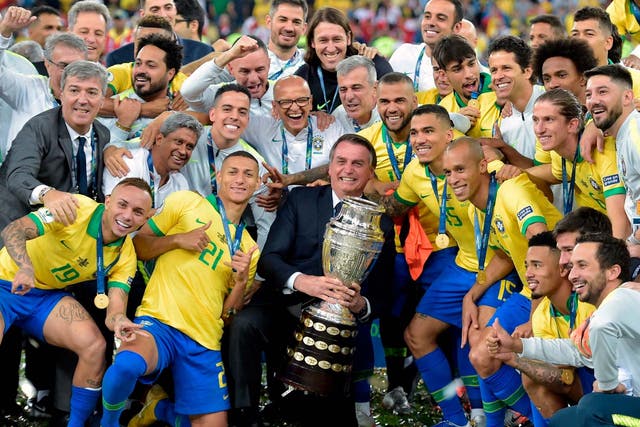 Brazilian president Jair Bolsonaro holds the Copa America trophy as members of the Brazilian national team celebrate