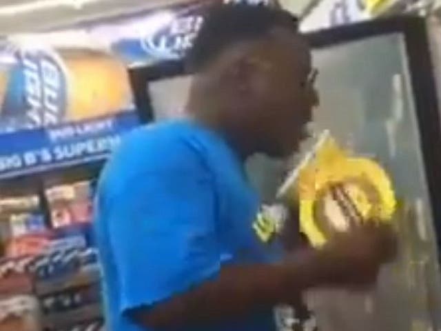 Still image from video of man licking ice cream from container before putting it back on shelf in supermarket freezer.