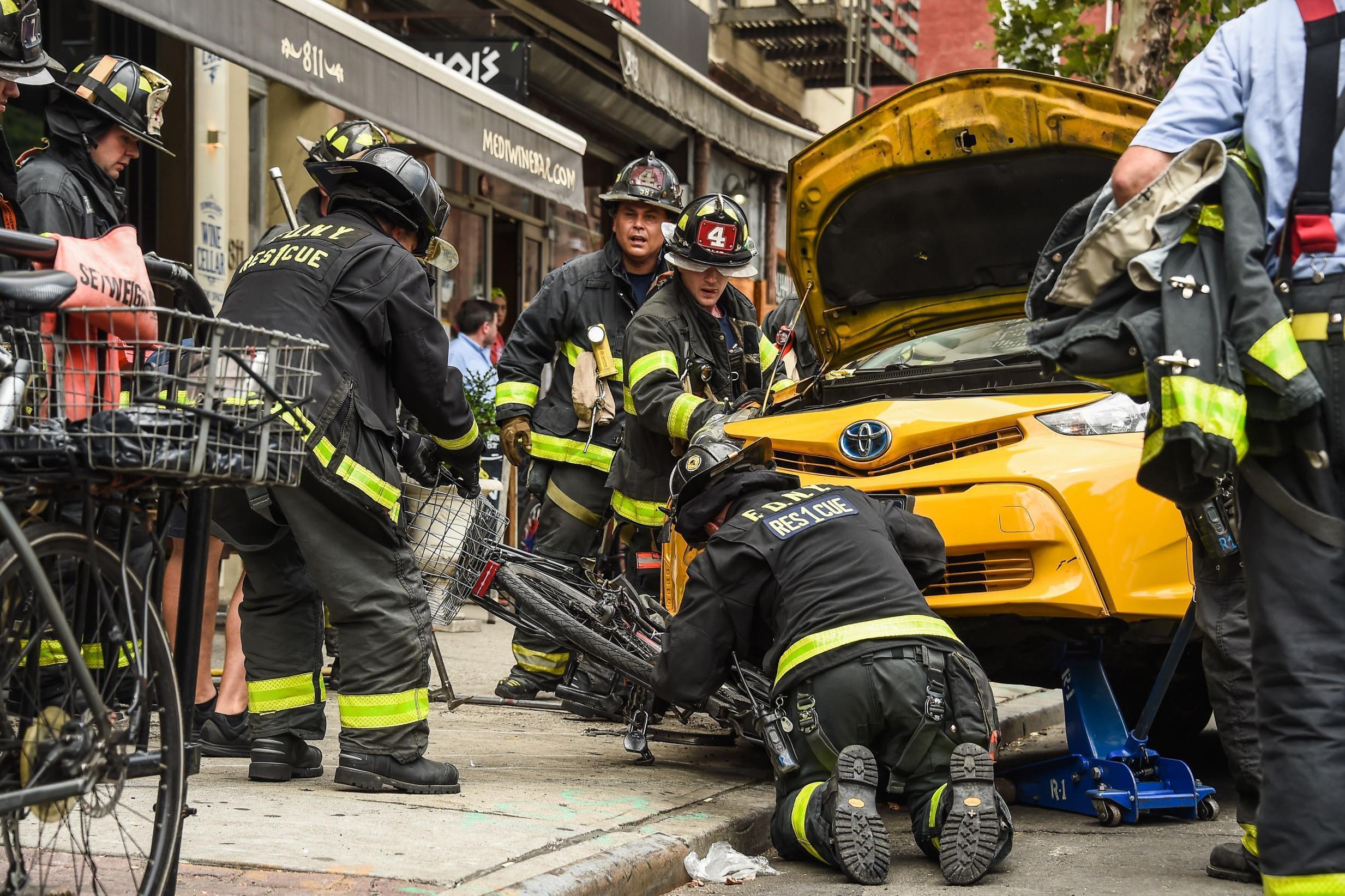 Firefighters work to remove the taxi from the curb in Hell's Kitchen