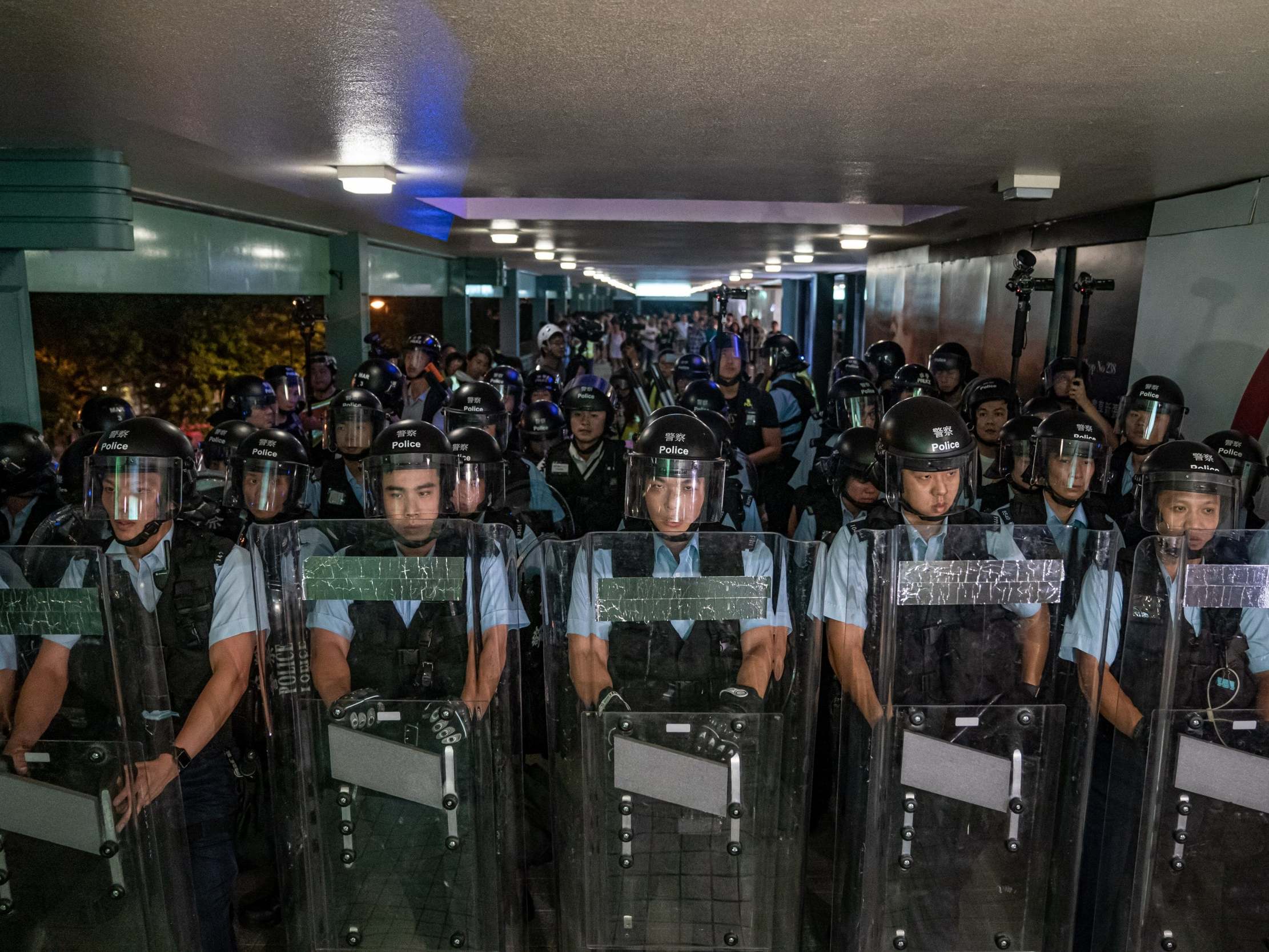 Police officers hold shields on a pedestrian bridge during stand-off with protesters after a rally in Sheung Shui