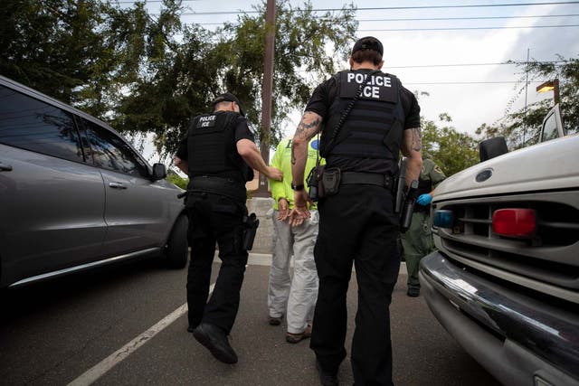 Immigration and Customs Enforcement (ICE) agents escort a man in handcuffs