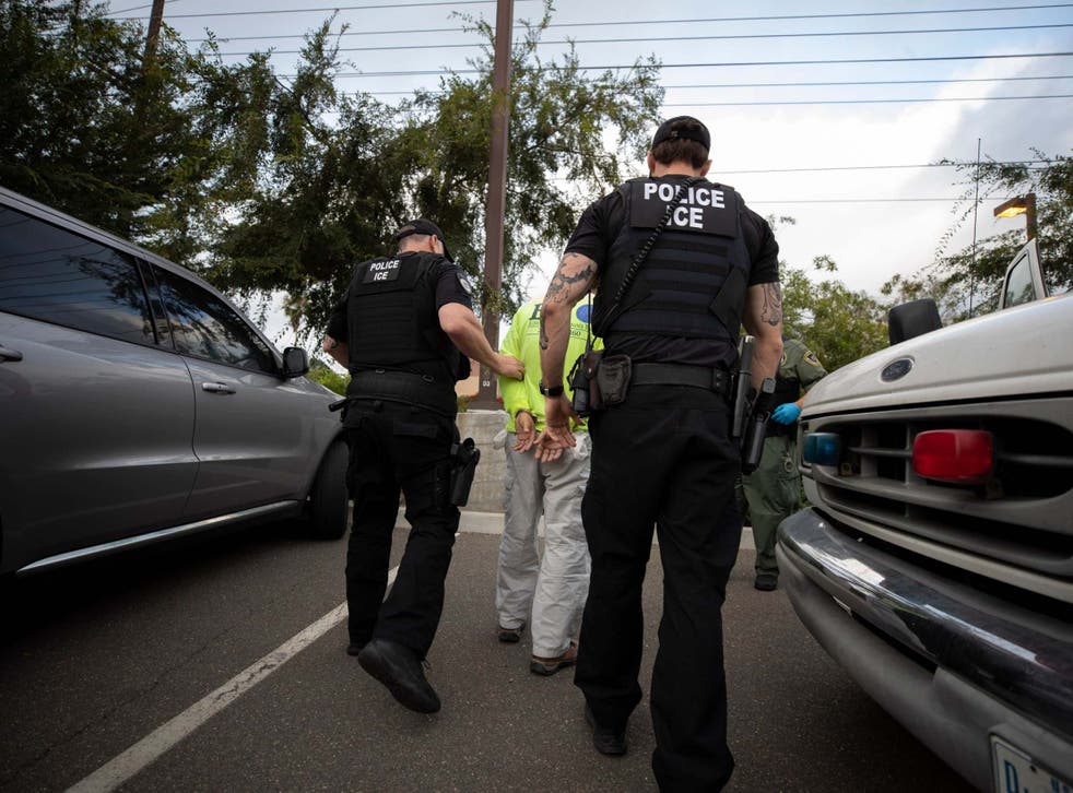 Immigration and Customs Enforcement (ICE) agents escort a man in handcuffs