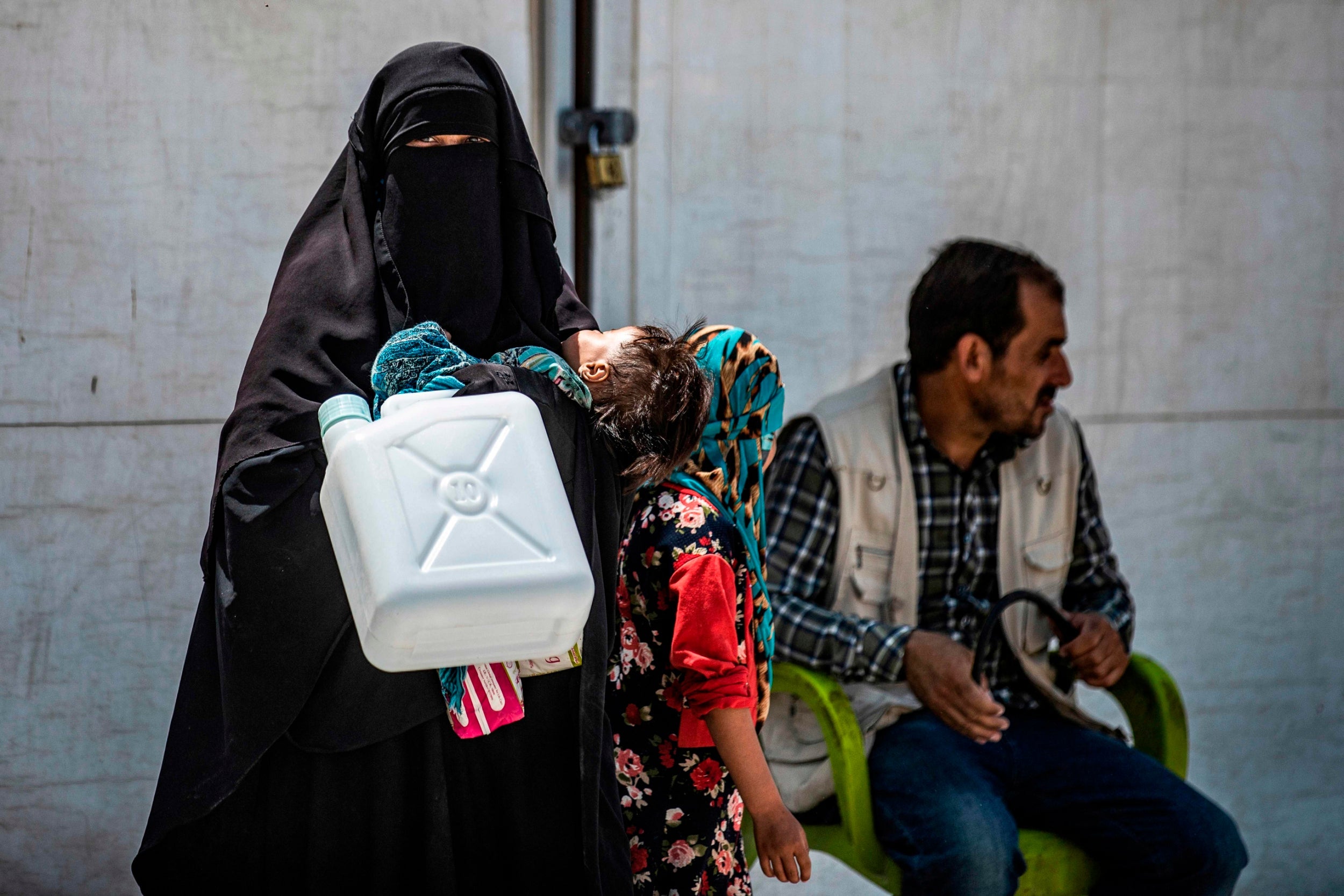 A woman carrying a jerry can and a toddler at al-Hol camp for displaced people northeastern Syria in July 2019