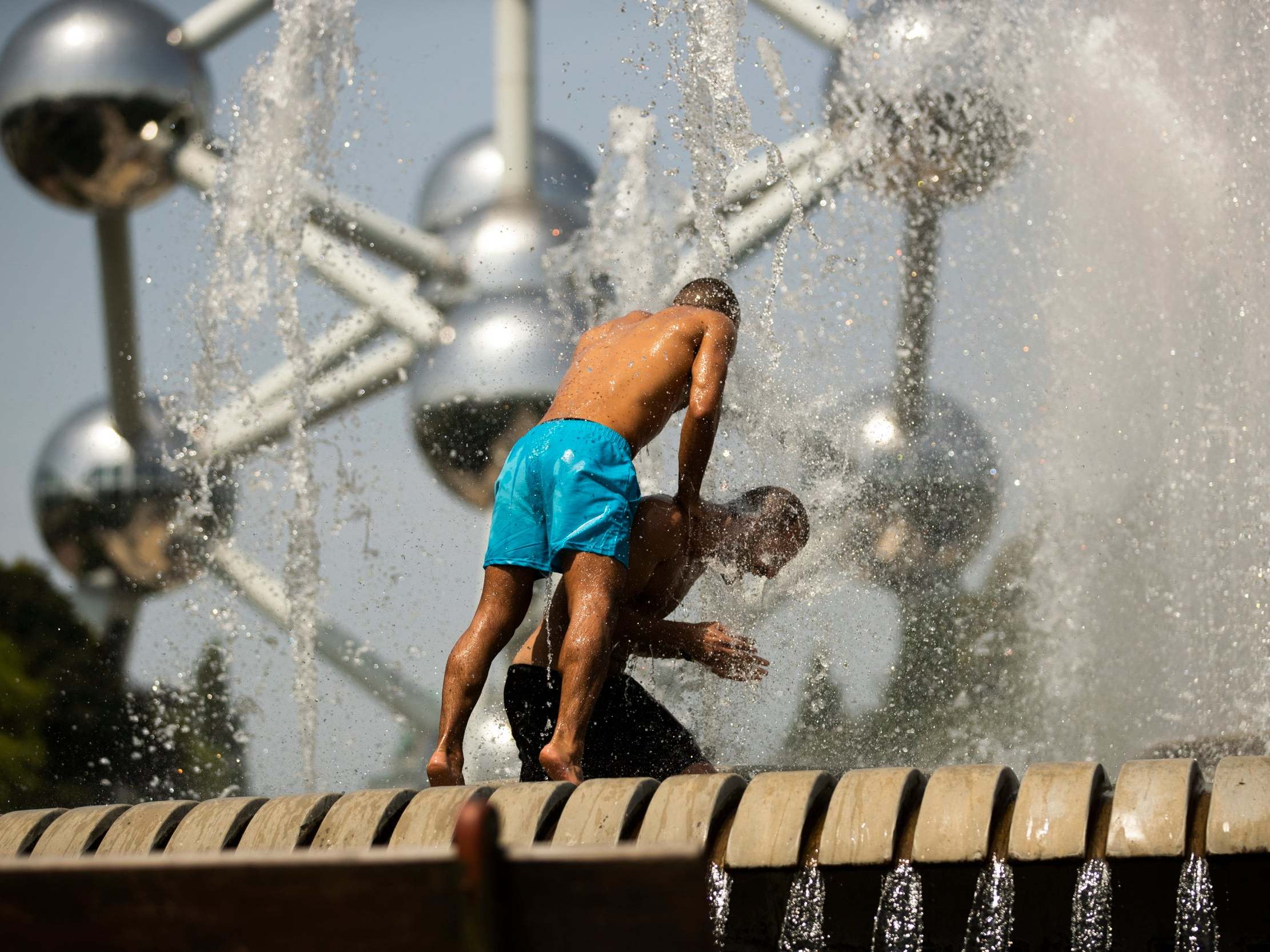 Men cool off in a public fountain near the Atomium in Brussels as parts of Europe see a record-breaking heat wave