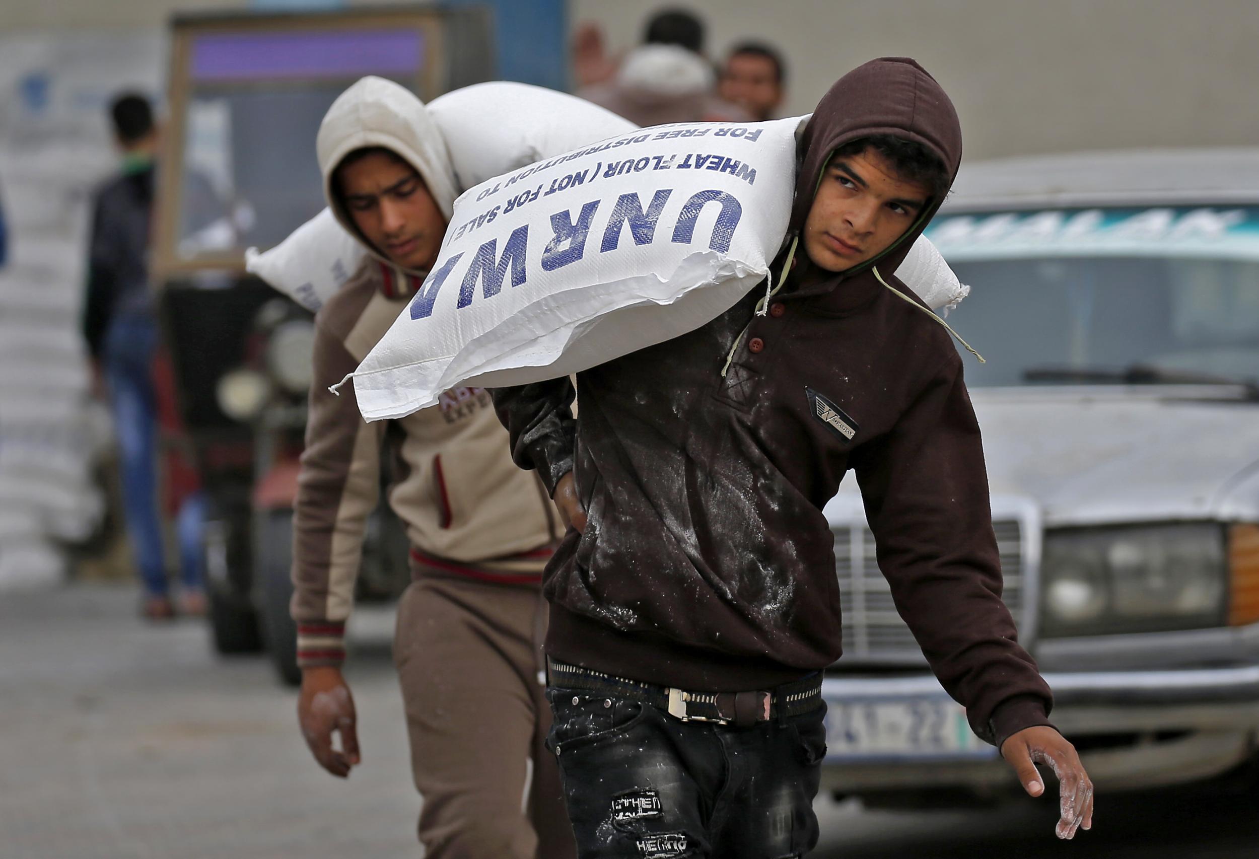 Palestinian men carry bags of flour outside an aid distribution centre run by UNRWA (Getty)