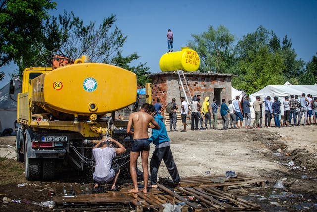 Residents of the camp wait in line for food distributed from Bihać Red Cross, while men wash themselves at the back of a water truck.
