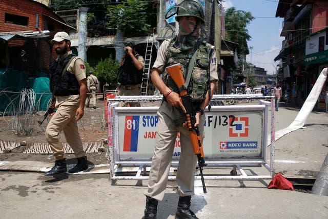 An Indian paramilitary soldier stands guard as policemen walk past in Srinagar on Friday