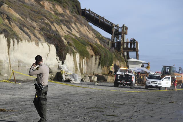 A San Diego County Sheriff's deputy looks on as search and rescue personnel work at the site of a cliff collapse