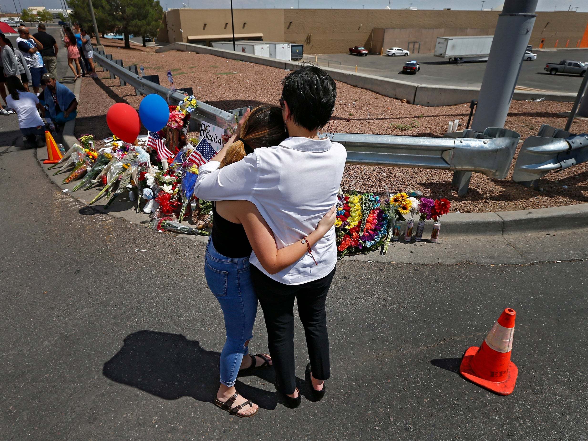 Two women hug and comfort each other while standing in front of a makeshift memorial along the street behind the scene of the mass shooting at a Walmart in El Paso