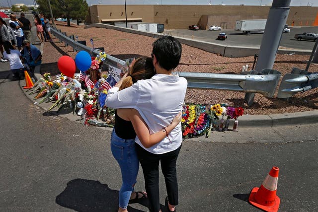 Two women hug and comfort each other while standing in front of a makeshift memorial along the street behind the scene of the mass shooting at a Walmart in El Paso