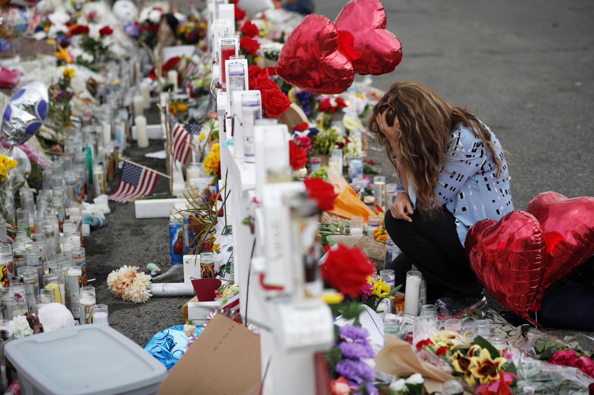 Gloria Garces kneels in front of crosses at a makeshift memorial near the scene of a mass shooting at a shopping complex Tuesday, Aug. 6, 2019, in El Paso, Texas