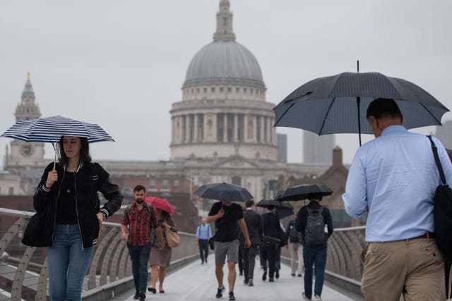 Pedestrians shelter under umbrellas as they cross the Millennium Bridge in central London