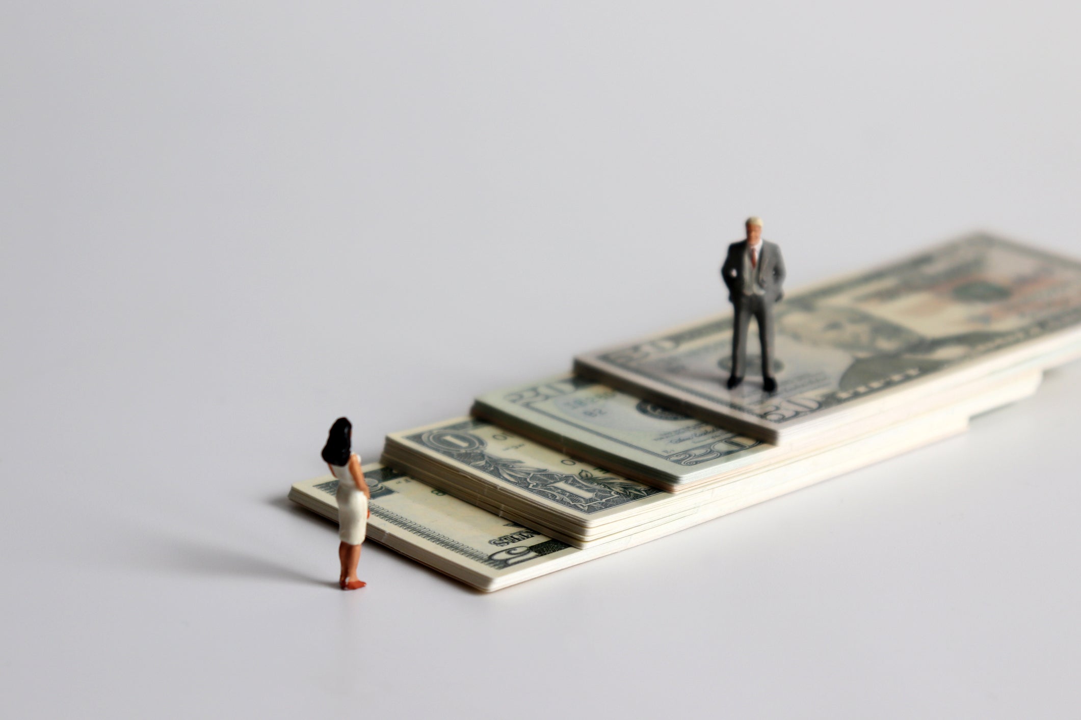 A miniature man and a miniature woman standing on a pile of bills