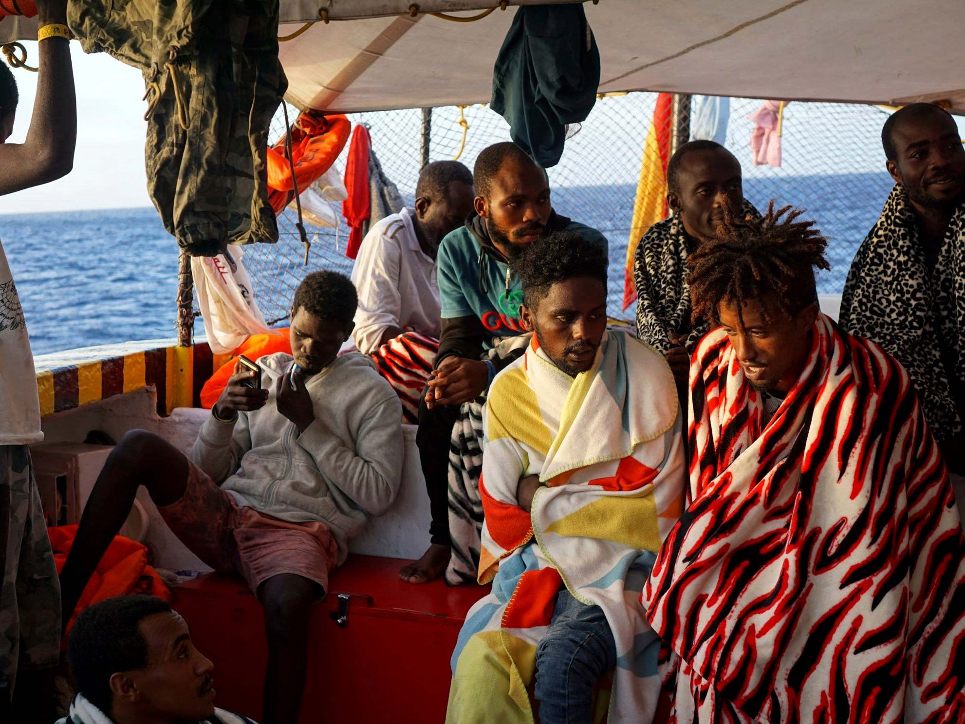 Migrants sit aboard the Open Arms as it arrives near Lampedusa coast in the Mediterranean Sea
