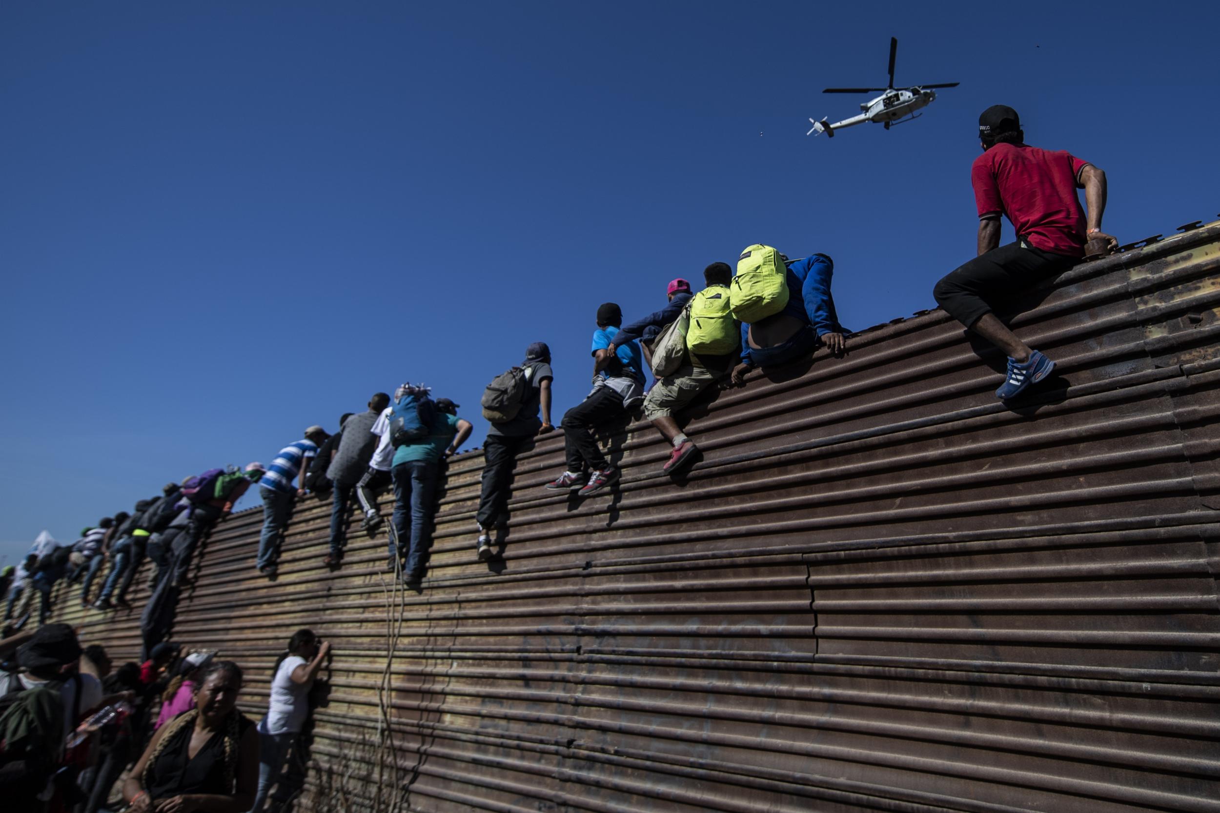 A group of Central American migrants climb a metal barrier on the Mexico-US border near El Chaparral border crossing in 2018.