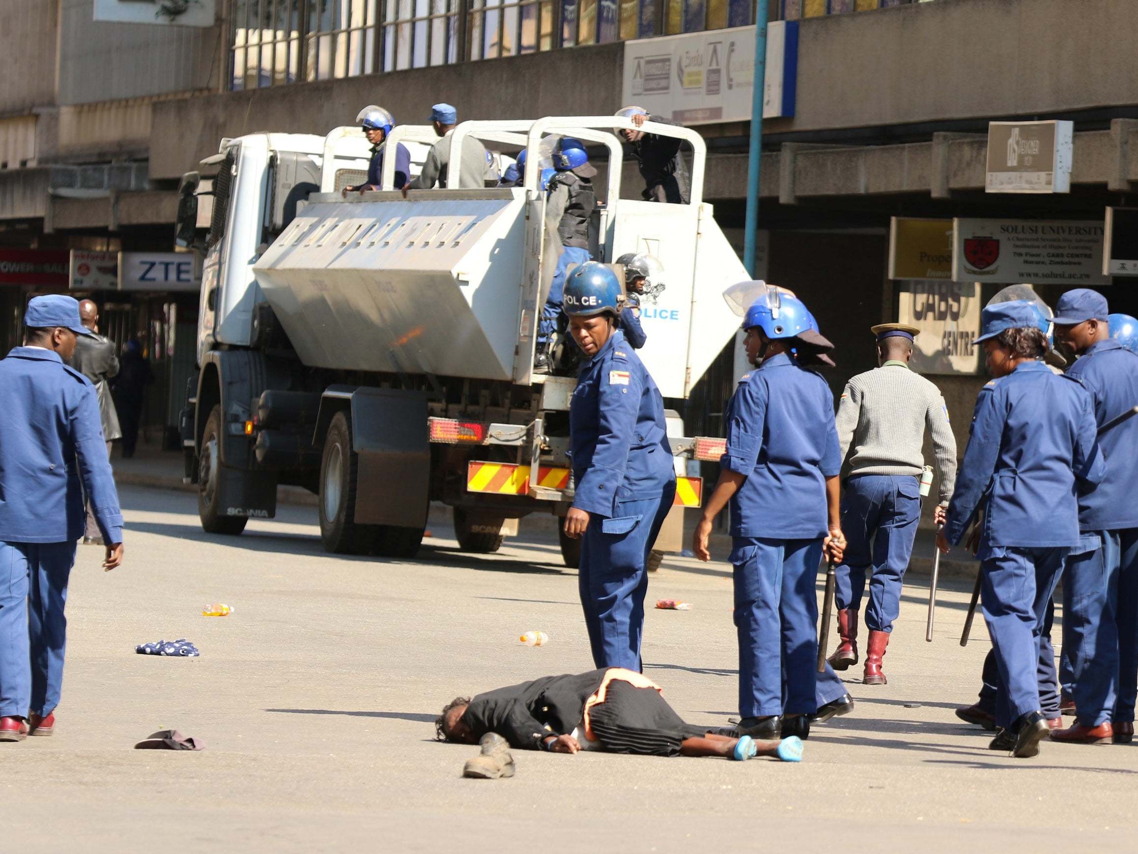 Police stand beside a woman injured woman during clashes in Harare